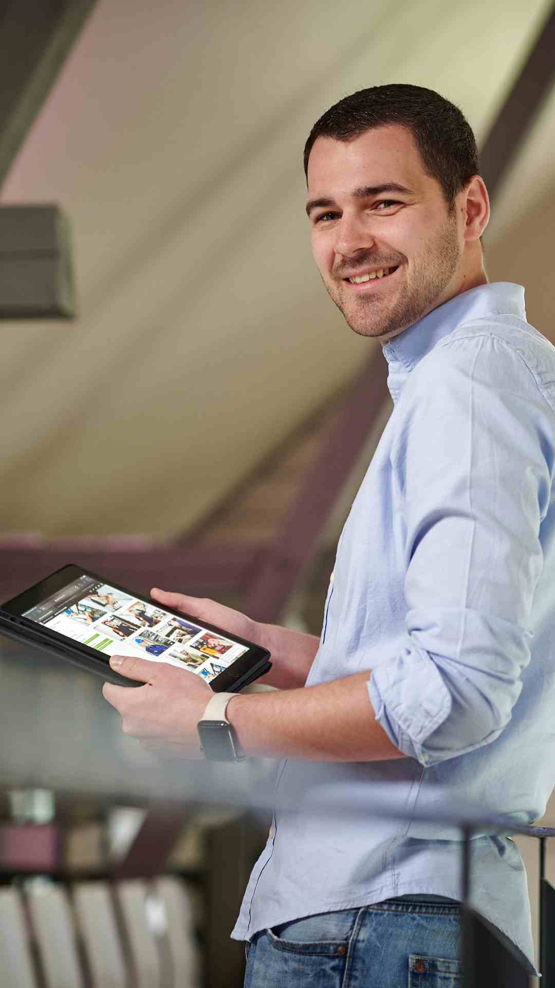 Bild von Marco, bei dem er ein Tablet in den Händen hält und dabei in die Kamera lächelt
